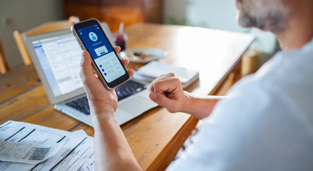Persoana verifica pe telefon o aplicatie bancara si situatia unei popriri ANAF, cu acte si laptop pe masa