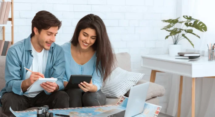 Cuplu care planifică bugetul de vacanță acasă, cu hartă, tabletă și laptop