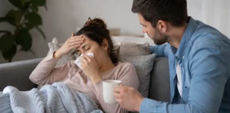 Concediu medical: cu cât stai mai puțin acasă, cu atât pierzi mai mult Femeie bolnavă acasă pe canapea, în concediu medical, îngrijită de partener