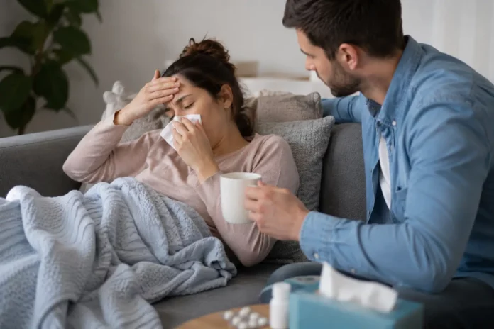 Femeie bolnavă acasă pe canapea, în concediu medical, îngrijită de partener
